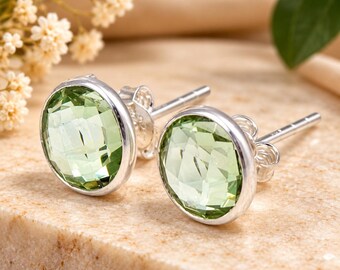 May include: A pair of round stud earrings featuring faceted light green stones set in polished silver-toned metal. Each earring has a circular bezel setting and a standard post back with a matching silver-toned butterfly clutch closure.