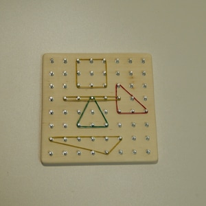 Puede incluir: Una tabla de madera con clavijas y gomas elásticas de colores que forman figuras geométricas, incluyendo un cuadrado, un triángulo y un rectángulo.