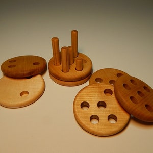 Puede incluir: Juguete de madera con cinco piezas redondas, cuatro con agujeros y una con clavijas. Las piezas son de madera marrón claro y tienen un acabado liso.