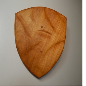 Peut inclure: Une plaque en bois en forme de bouclier avec une finition en bois naturel. La plaque a deux petits trous percés.