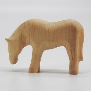 May include: A wooden horse figurine with a light brown color. The horse is standing on all four legs and has its head lowered as if it is grazing.