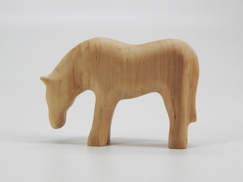 May include: A wooden horse figurine with a light brown color. The horse is standing on all four legs and has its head lowered as if it is grazing.