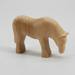 May include: A wooden horse figurine with a light brown color and a smooth, polished finish. The horse is standing with its head lowered, as if it is grazing.
