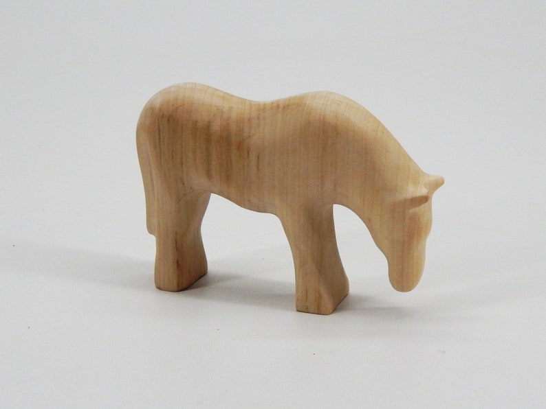 May include: A wooden horse figurine with a light brown color and a smooth, polished finish. The horse is standing with its head lowered, as if it is grazing.