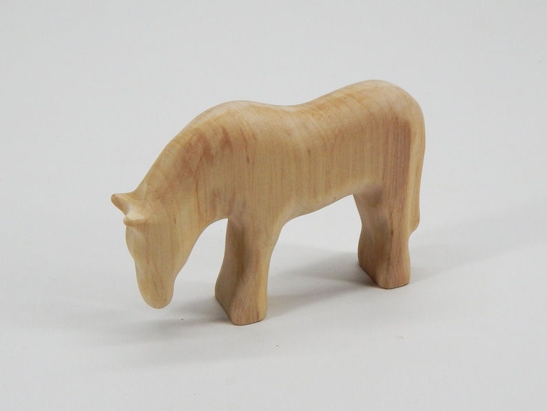 May include: A wooden horse figurine with a light brown color. The horse is standing with its head lowered as if it is grazing.