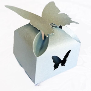 May include: A light blue favor box with a silver butterfly on top. The box has a cut-out butterfly shape on the front.