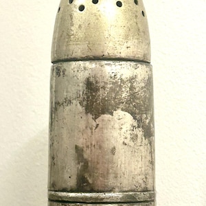 May include: A silver metal salt shaker shaped like a bullet with a perforated top. The shaker has a worn, aged appearance.