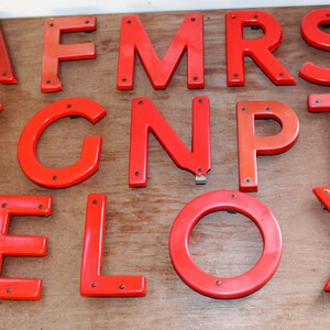 Pu&ograve; includere: Lettere in plastica rossa dell'alfabeto, A, F, M, R, S, C, G, N, P, T, E, L, O, X, su una superficie di legno.