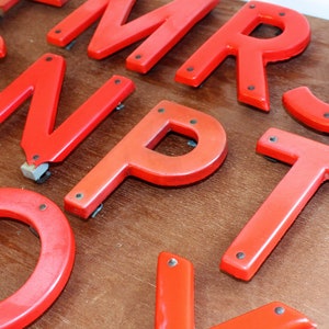 Pu&ograve; includere: Lettere dell'alfabeto in plastica rossa, tra cui le lettere M, R, S, N, P, T e O. Le lettere sono su una superficie di legno.