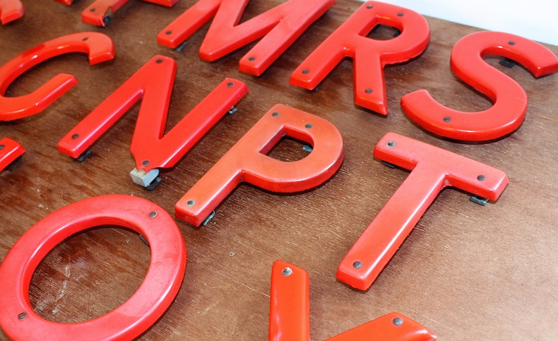 Pu&ograve; includere: Lettere dell'alfabeto in plastica rossa, tra cui le lettere M, R, S, N, P, T e O. Le lettere sono su una superficie di legno.