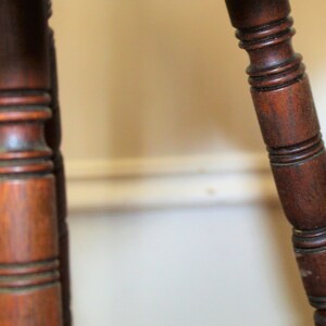 May include: Close-up of two dark brown wooden table legs with intricate carvings. The legs are turned and have a smooth, polished finish.