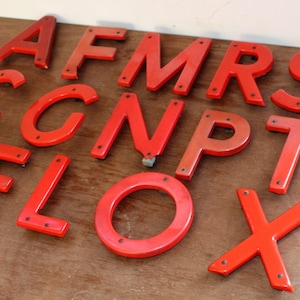 Pu&ograve; includere: Un set di lettere in plastica rossa, tra cui le lettere A, F, M, R, S, C, G, N, P, T, E, L, O e X. Le lettere sono tutte maiuscole e hanno un aspetto leggermente usurato.