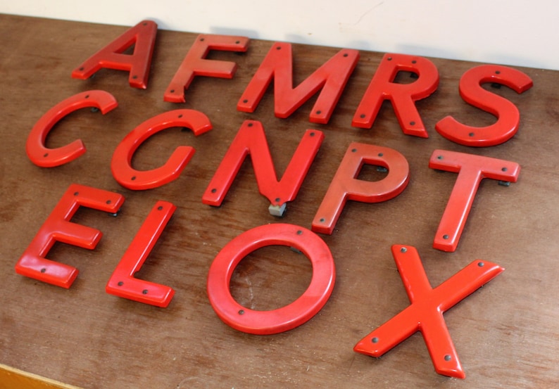 Pu&ograve; includere: Un set di lettere in plastica rossa, tra cui le lettere A, F, M, R, S, C, G, N, P, T, E, L, O e X. Le lettere sono tutte maiuscole e hanno un aspetto leggermente usurato.