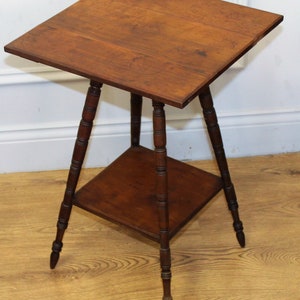 May include: A wooden side table with a square top and a lower shelf. The table has three turned legs with decorative details.
