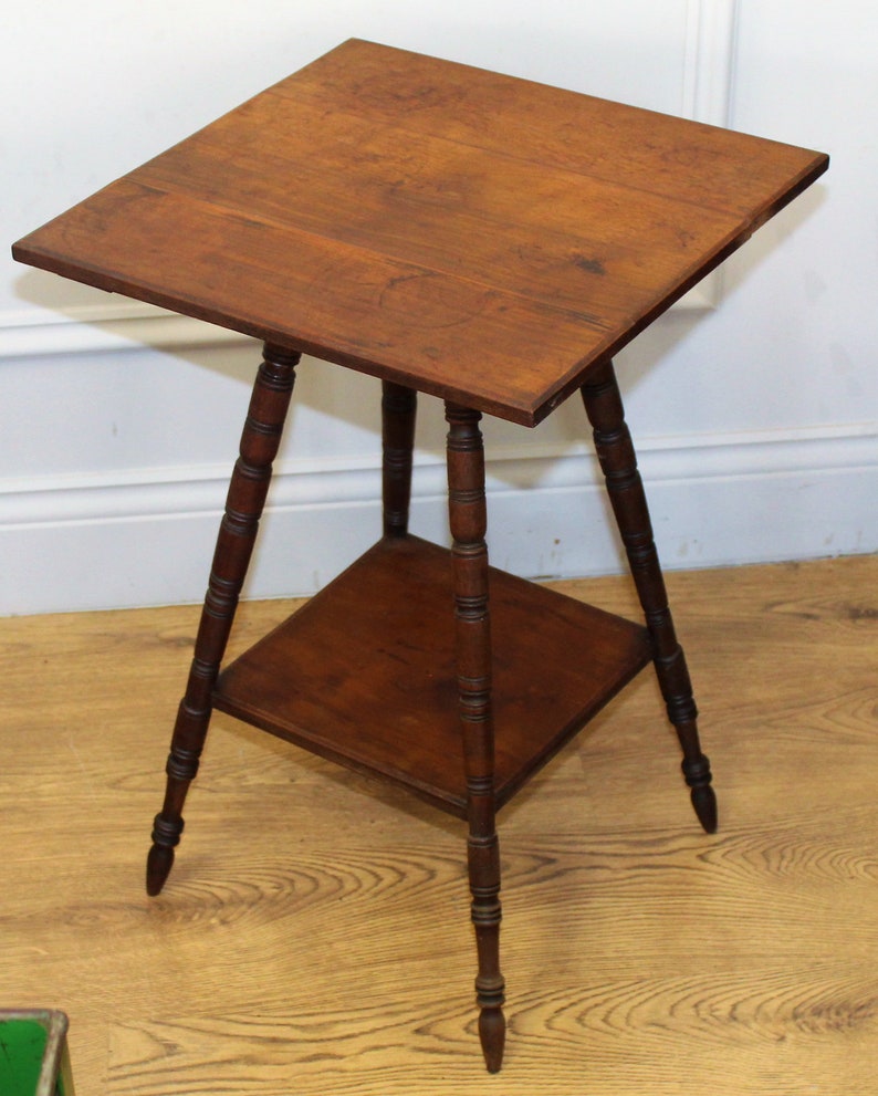 May include: A wooden side table with a square top and a lower shelf. The table has three turned legs with decorative details.