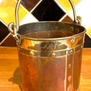 May include: A small copper and brass bucket with a brass handle. The bucket has a hammered copper finish and is decorated with brass rivets.