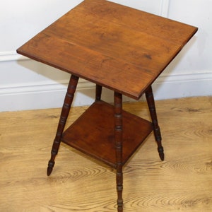 May include: A wooden side table with a square top and a lower shelf. The table has four turned legs with a decorative design.