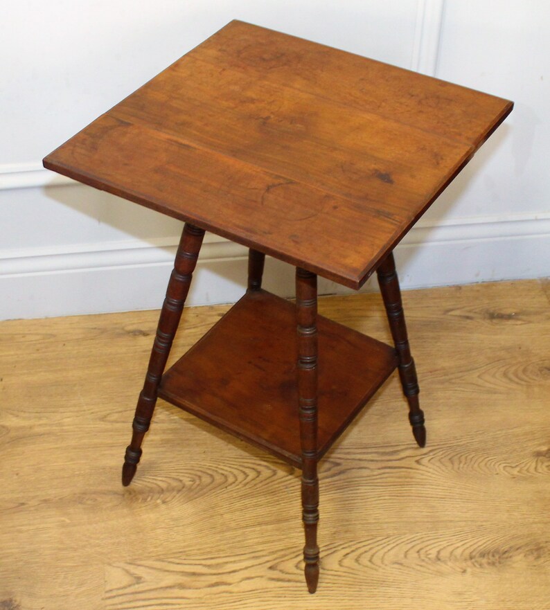 May include: A wooden side table with a square top and a lower shelf. The table has four turned legs with a decorative design.