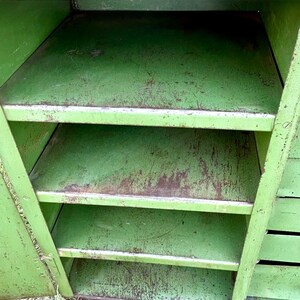 K&ouml;nnte beinhalten: Ein offener, gr&uuml;ner Vintage-Metallschrank mit vier Regalen. Der Schrank hat eine abgenutzte Oberfl&auml;che, die Gebrauchsspuren aufweist. Die Regale sind gleichm&auml;&szlig;ig angeordnet. Der Schrank wird wahrscheinlich zur Aufbewahrung verwendet.