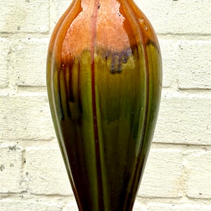 May include: A tall, decorative vase with a fluted rim and a flared base. The vase features a gradient of colours, transitioning from a warm brown at the top to a deep green at the base. Vertical streaks of darker hues add depth to the design.
