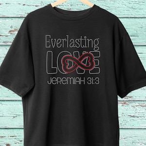 May include: Black t-shirt with the words "Everlasting LOVE" in a rhinestone design. The infinity symbol is red and the text "JEREMIAH 31:3" is below the word LOVE. The shirt is hanging on a wooden hanger.