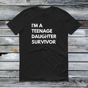 Puede incluir: Camiseta negra con texto blanco que dice "Soy una hija adolescente superviviente".