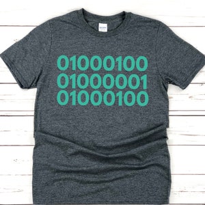 May include: A dark gray t-shirt with a teal green design of the binary code "01000100 01000001 01000100".