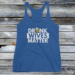Op de afbeelding: Een blauw tanktop met een witte afbeelding waarop "DRUNK WIVES MATTER" staat, met een cartoon-bierglas boven het woord "DRUNK".