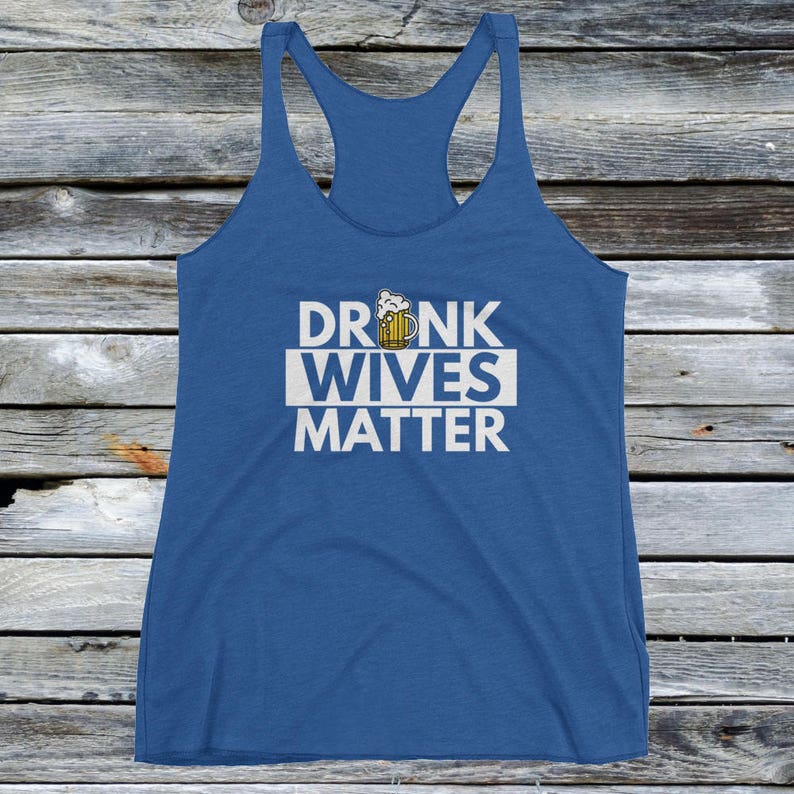 Op de afbeelding: Een blauw tanktop met een witte afbeelding waarop "DRUNK WIVES MATTER" staat, met een cartoon-bierglas boven het woord "DRUNK".