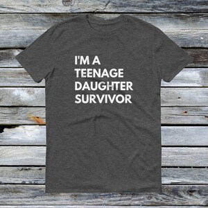 Puede incluir: Una camiseta gris oscuro jaspeada con el texto "I'm a Teenage Daughter Survivor" impreso en blanco.