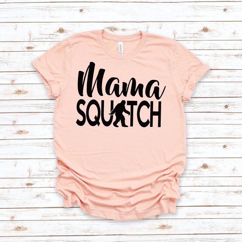 May include: A peach-coloured t-shirt with black text that reads "Mama Squatch" and a black silhouette of Bigfoot walking.