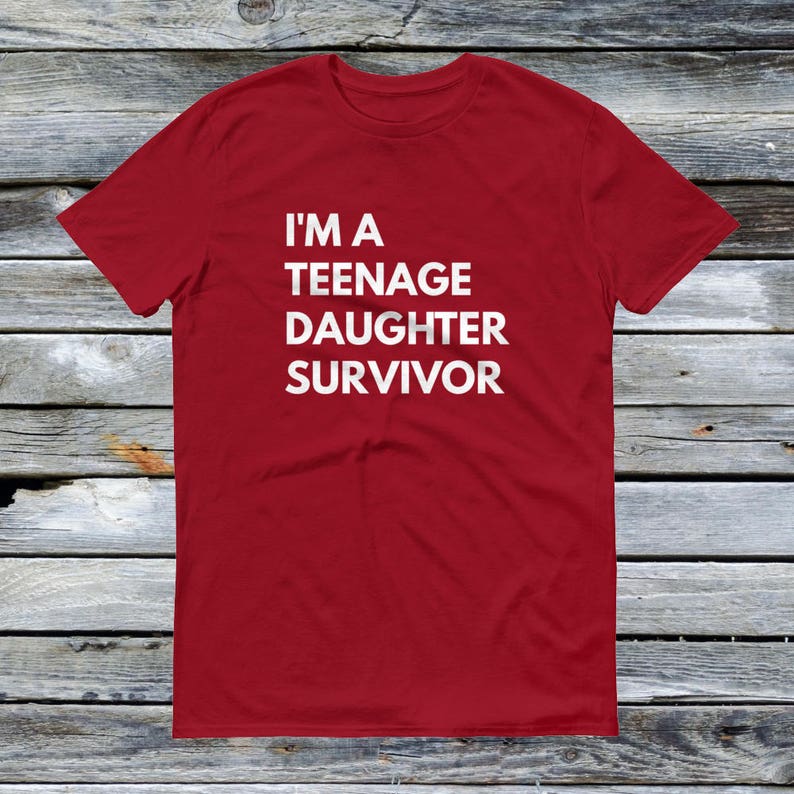 Puede incluir: Camiseta roja con texto blanco que dice "Soy una sobreviviente de una hija adolescente".