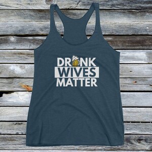 Op de afbeelding: Een donkerblauw tanktop met een witte afbeelding waarop "DRUNK WIVES MATTER" staat met een cartoon bierglas boven de tekst.