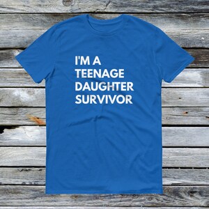 Puede incluir: Una camiseta azul real con texto blanco que dice "Soy una sobreviviente de una hija adolescente".