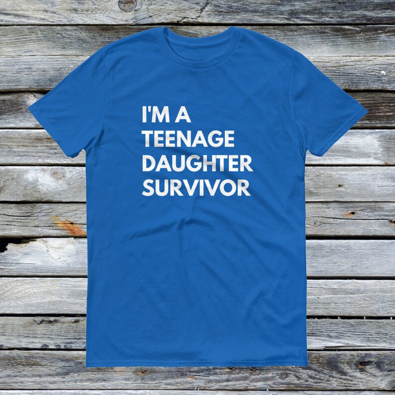 Puede incluir: Una camiseta azul real con texto blanco que dice "Soy una sobreviviente de una hija adolescente".