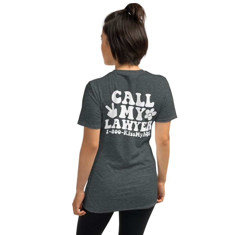 May include: A dark heather grey t-shirt with a white graphic that says "Call My Lawyer" with a peace sign and a flower. The phone number 1-800-KissMyA** is printed below the graphic.