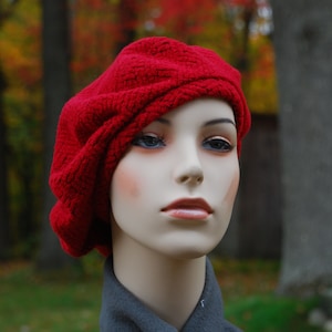 May include: A red knitted beret with a textured surface. The beret is worn on a mannequin's head.