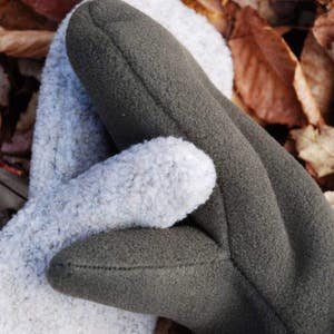 May include: A pair of fleece mittens, one is grey and the other is dark green. The mittens are made of a soft, fuzzy material.