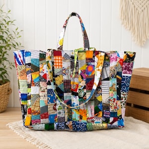 May include: A large tote bag constructed from a patchwork of various colorful fabric strips. The bag features a rectangular shape with two fabric handles and a multi-patterned design including floral, geometric, and animal prints in many colors.