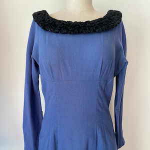 Peut inclure: Robe vintage bleue avec des manches longues et un col texturé noir. La robe a un corsage ajusté et une jupe droite, mettant en valeur une silhouette classique. La robe est présentée sur un mannequin.