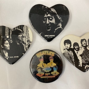 Puede incluir: Una colección de cuatro botones vintage de los Beatles y John Lennon. Dos pines en forma de corazón presentan imágenes de John Lennon y Yoko Ono, y los Beatles. Un pin redondo conmemora el 25 aniversario de los Beatles.