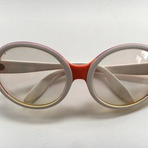 May include: White and orange round framed glasses with clear lenses.