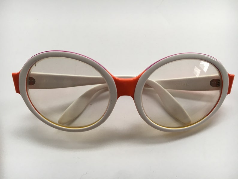 May include: White and orange round framed glasses with clear lenses.