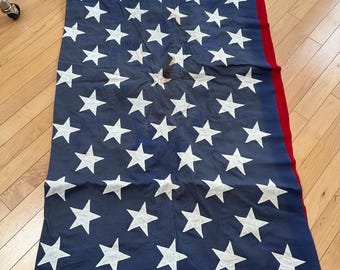 Può includere: Una bandiera americana rettangolare con un cantone blu con stelle bianche e strisce orizzontali rosse e bianche. La bandiera presenta una striscia di intestazione bianca lungo un bordo con un occhiello metallico visibile nell'angolo.
