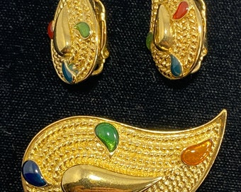 May include: A gold-tone teardrop-shaped brooch with a textured surface and colorful enamel accents. The brooch is accompanied by a pair of matching earrings.