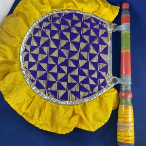 May include: A decorative hand fan with a yellow ruffled border and a purple and gold patterned center. The handle is painted with red, green, and yellow stripes. The fan is made of fabric and wood.
