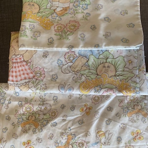 May include: Three white fabric pillowcases with a Cabbage Patch Kids theme. The pillowcases feature a white background with colorful flowers, butterflies, and Cabbage Patch Kids characters. The text "Cabbage Patch Kids" is printed on two of the pillowcases.