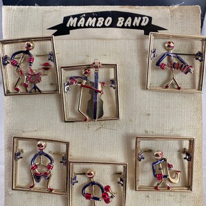 May include: Six gold-toned metal pins depicting stick figures playing musical instruments. Each pin is framed in a square with musical notes. The pins are labeled "Mambo Band".