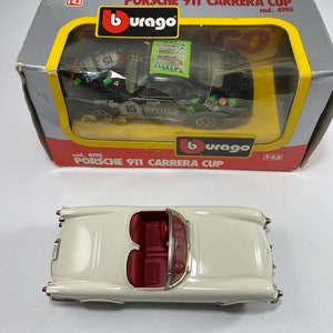 Könnte beinhalten: Ein weißes Burago-Spielzeugautomodell eines Porsche 911 Carrera Cup. Das Auto befindet sich in einer Schachtel mit dem Burago-Logo und dem Aufdruck "Porsche 911 Carrera Cup".