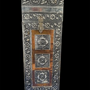 May include: A rectangular vertical storage box featuring a metallic silver-toned frame with embossed floral and vine patterns. The center panel is a warm copper-toned surface containing three square silver-toned plaques with lotus motifs.